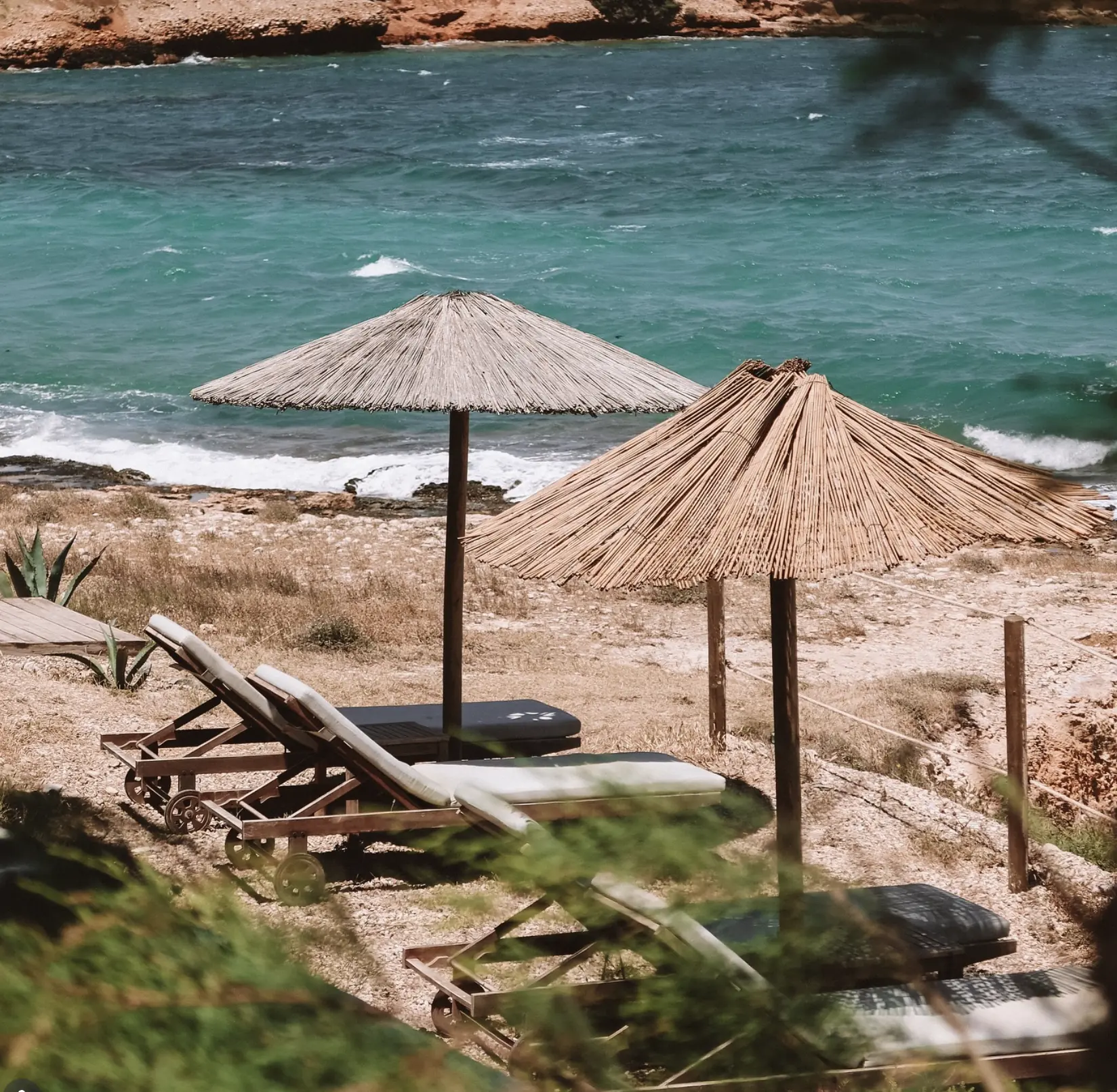 Thatched umbrellas on the small sandy beach beside Paros Comfy Suites at Xifara