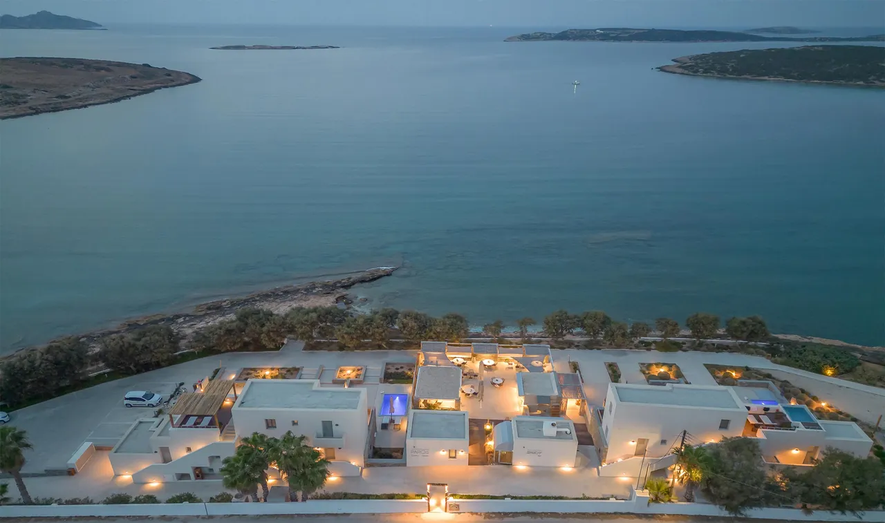 Paros Comfy Suites at dusk, lit up on its peninsula with Naoussa bay beyond