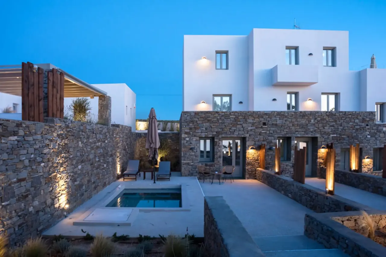 Stone-walled courtyards and private pools of the suites at Paros Comfy Suites, lit up at dusk